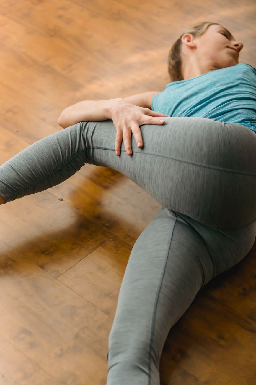 High angle of slim female lying on parquet of light studio and stretching leg aside