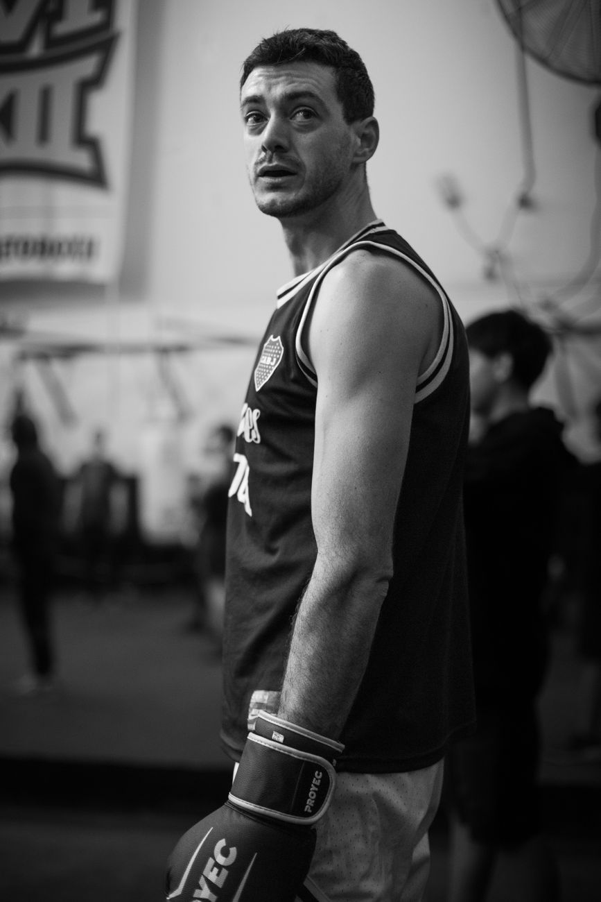 Black and white portrait of a male boxer wearing gloves in a Buenos Aires gym.