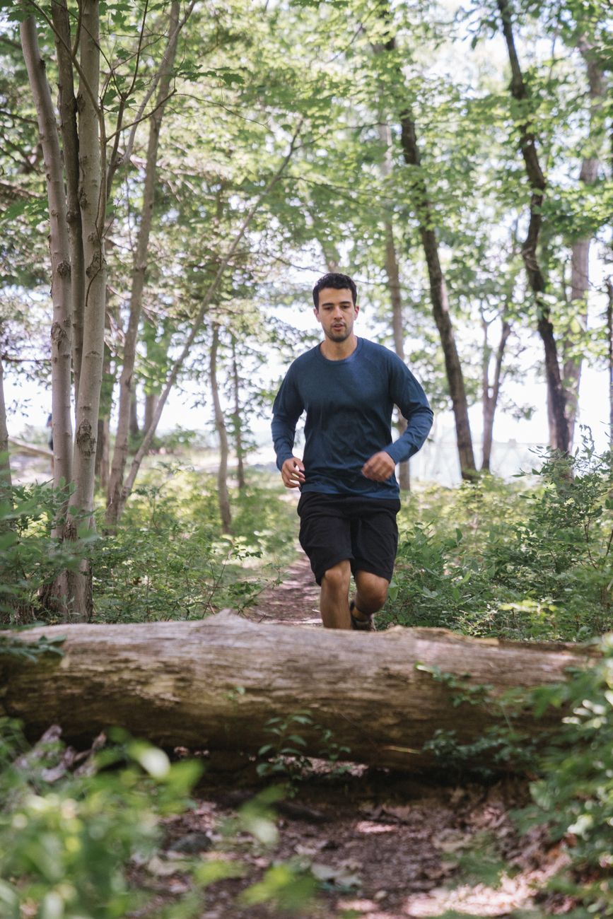 A man runs on a forest path, leaping over a large fallen tree trunk. Outdoor fitness.